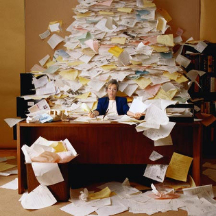 A woman at a desk with a huge pile of papers behind her