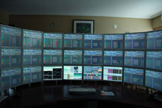 A computer desk containing a 3-by-8 grid of monitors