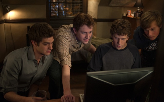 Four characters gathered around a computer from an early scene of the film The Social Network